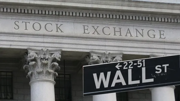 Sign reads "wall street" with "stock exchange" engraved on a building in the background.