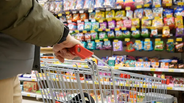 A man with a shopping cart stands in front of the sweets display case in a supermarket