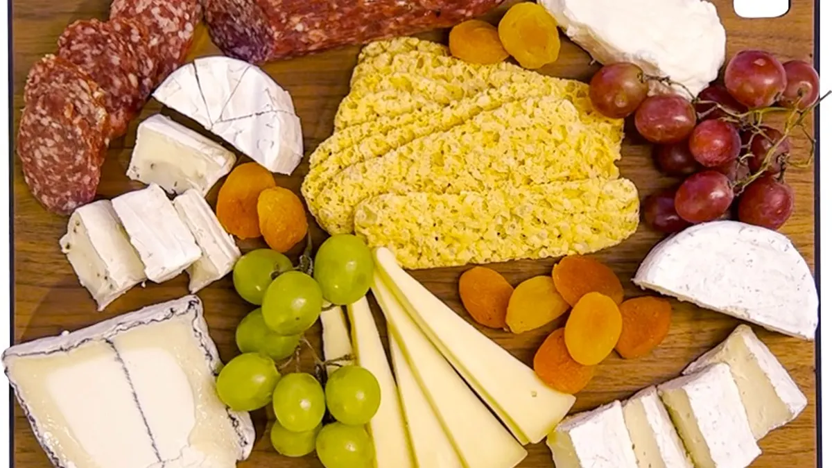 Cutting board displaying a variety of cheeses, crackers and grapes