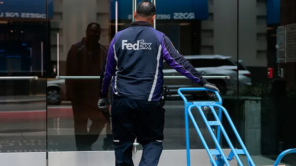 A person in a FedEx uniform enters a building while pulling a cart.