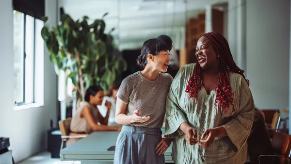 Two coworkers sharing a joyful moment and laughing together during a break in a modern office environment.