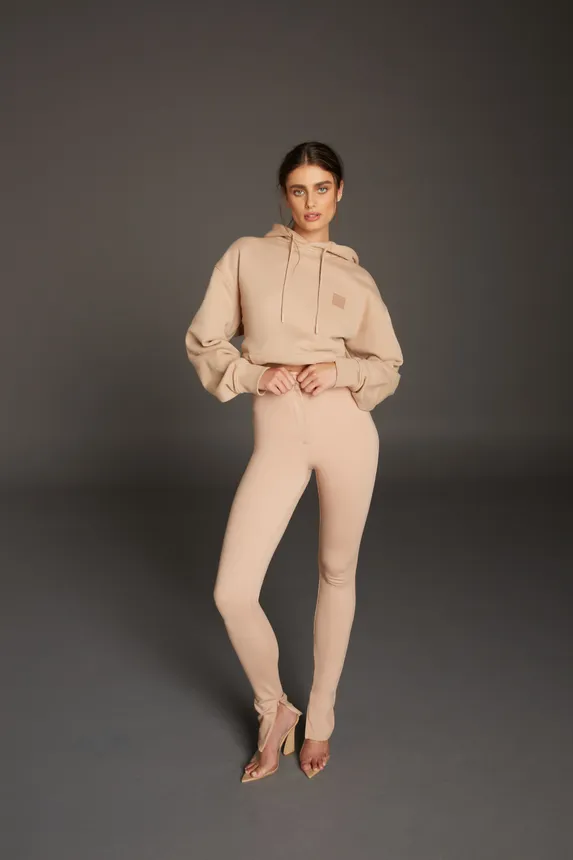 A person in a tan knit tight fitting sweatsuit and heels stares at the camera.