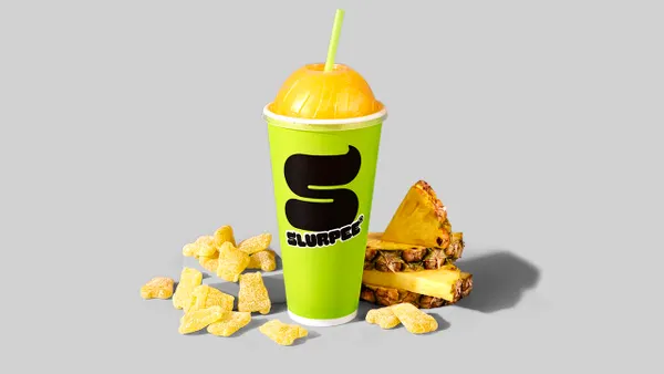 A cup full of a frozen beverage with gummies and other snacks around it against a gray background.