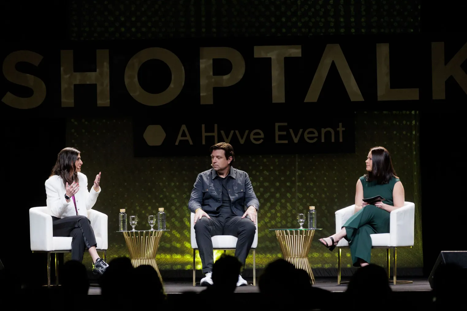 Three people sit on chairs on a stage with the word "Shoptalk" in the background.