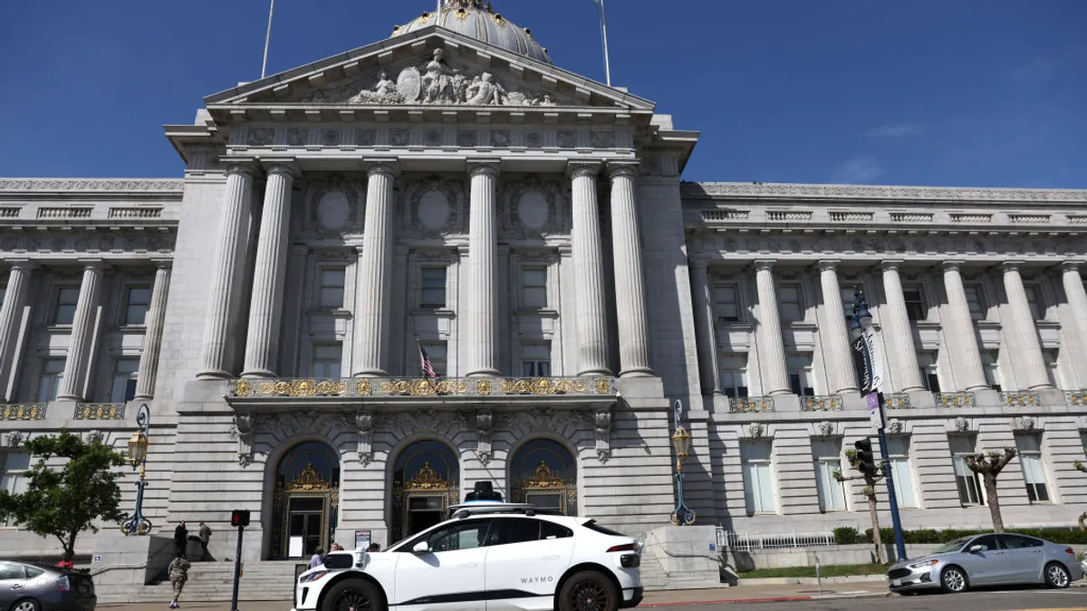 A Waymo autonomous vehicle passes in front of San Francisco City Hall