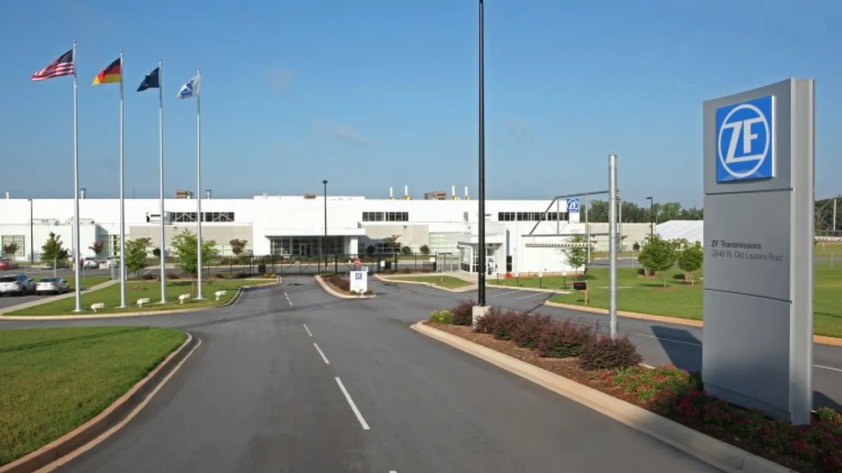 A white building with grass and a road in front of it, and a gray ZF sign on the right.