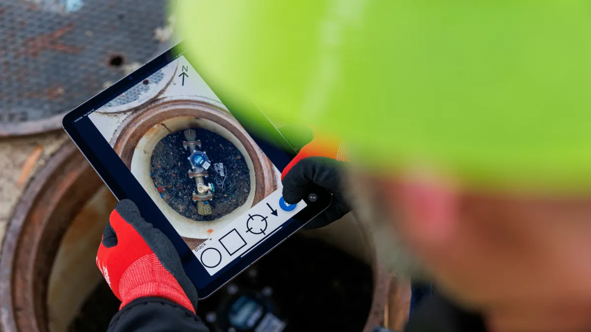 Zoomed in shot of a person with a hard hat on hold an ipad over a drain taking a scan.