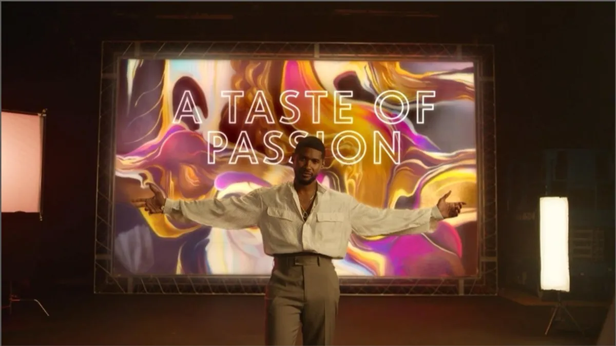 The musician Usher stands with his arms outstretched in front of a screen bearing the words, "A Taste of Passion."