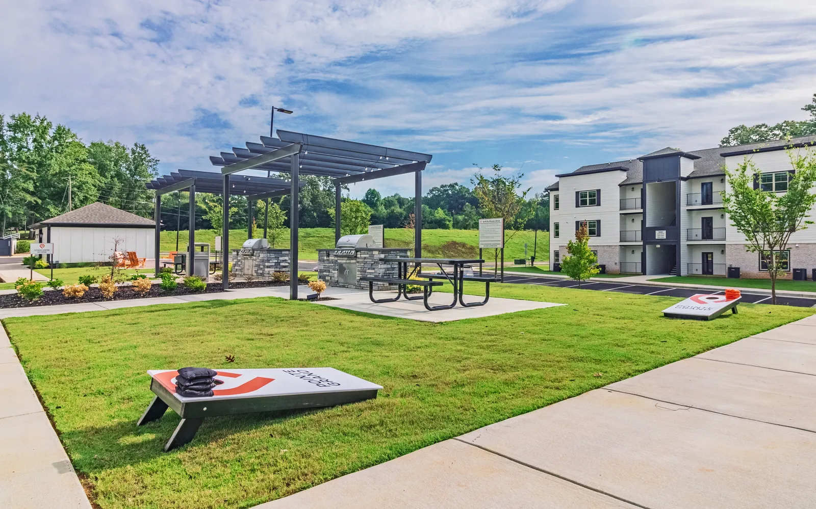 A lawn with grills and cornhole sets.