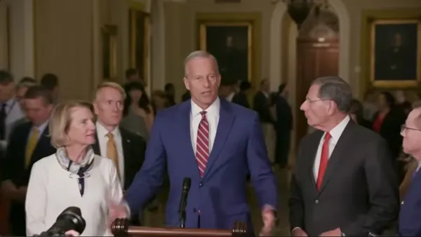 Person in blue suit at a podium surrounded by people beside and behind.