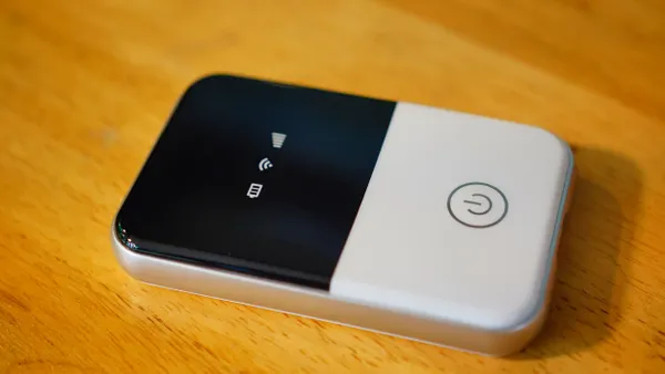 A modern wireless pocket 4g wi-fi modem sits on a wooden desk.