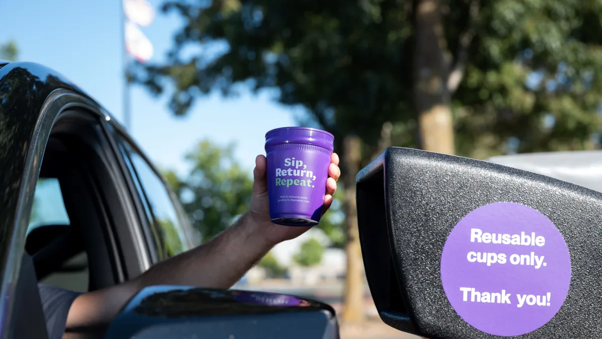 A reusable cup out a car window at a drive-through