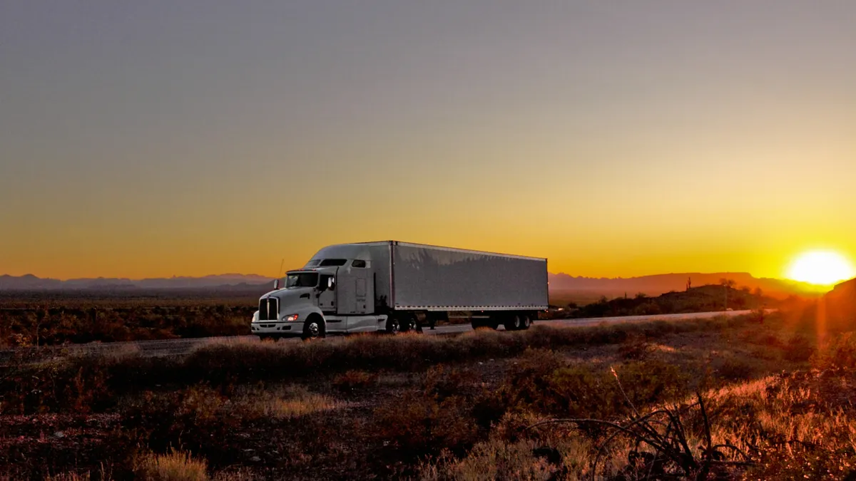 A tractor-trailer on a desert-doted road.