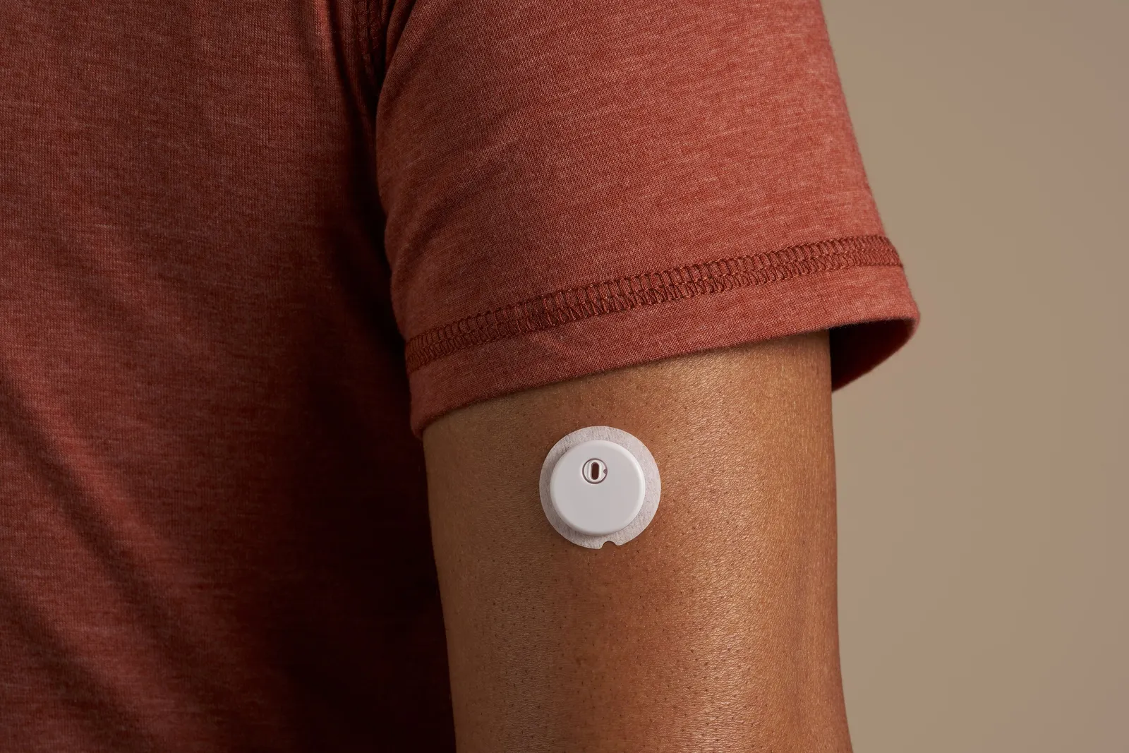 A white, round device is stuck on a person's arm below their sleeve.
