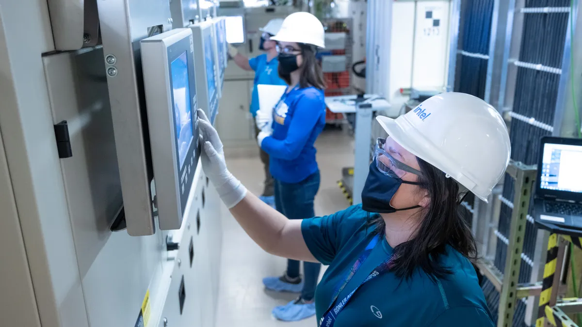 Three people wearing protective gear in a factory.