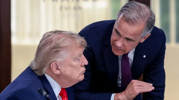 Canada Prime Minister Mark Carney leans over to speak to a seated U.S. President Donald Trump.