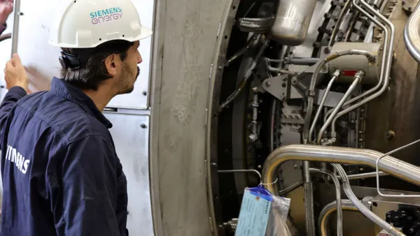 A technician wearing a Siemens Energy hard hat looks at a gas turbine.