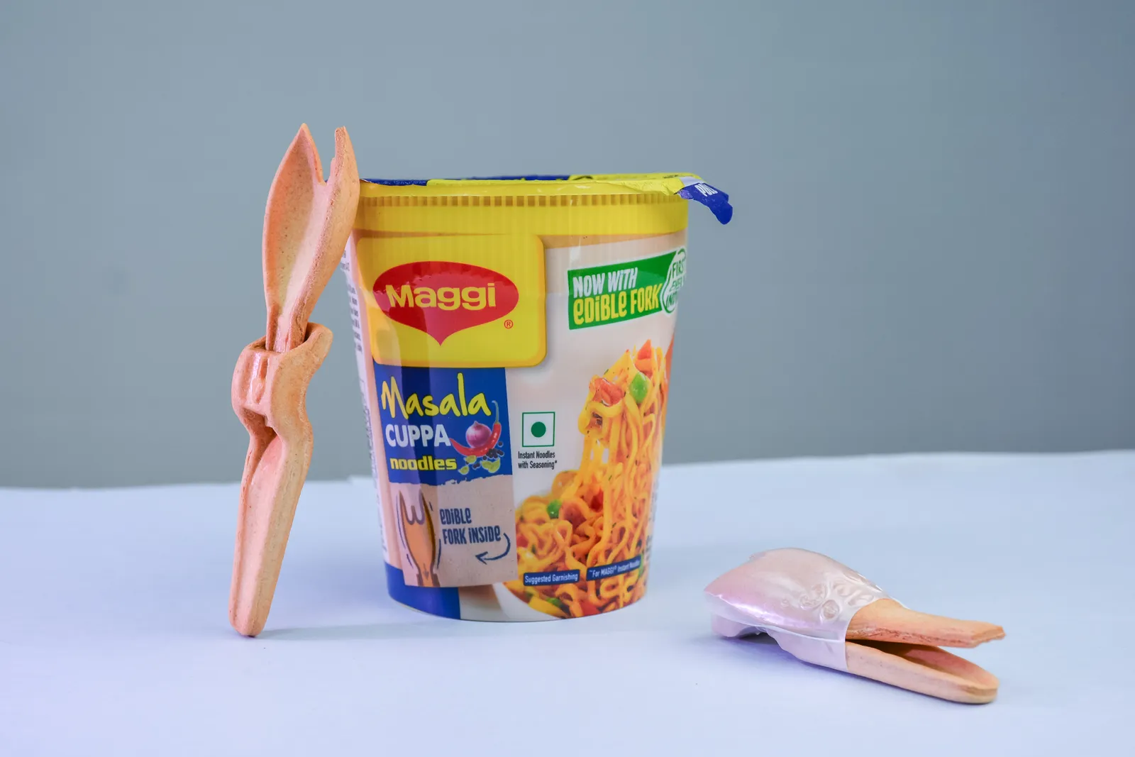 A container of Maggi cup noodles next to a beige-colored edible fork.