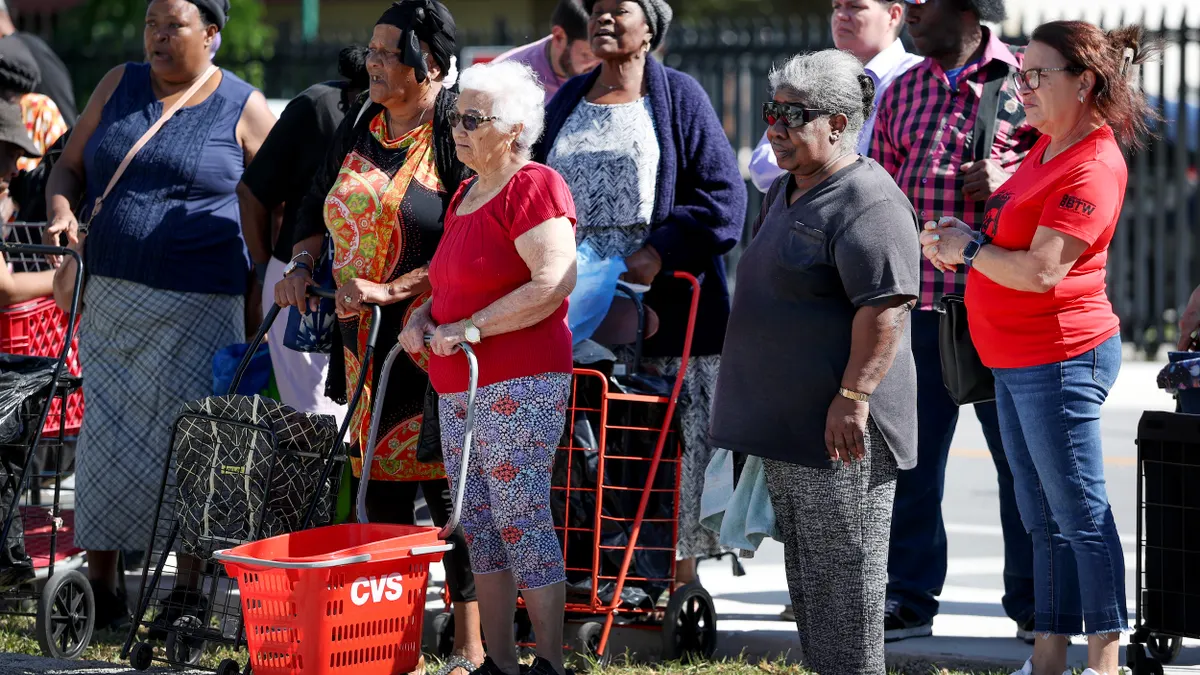 A group of people standing outside with grocery carts and baskets.