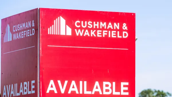 A large red advertisement poster that reads "Cushman & Wakefield, AVAILABLE" with a blue sky behind it.