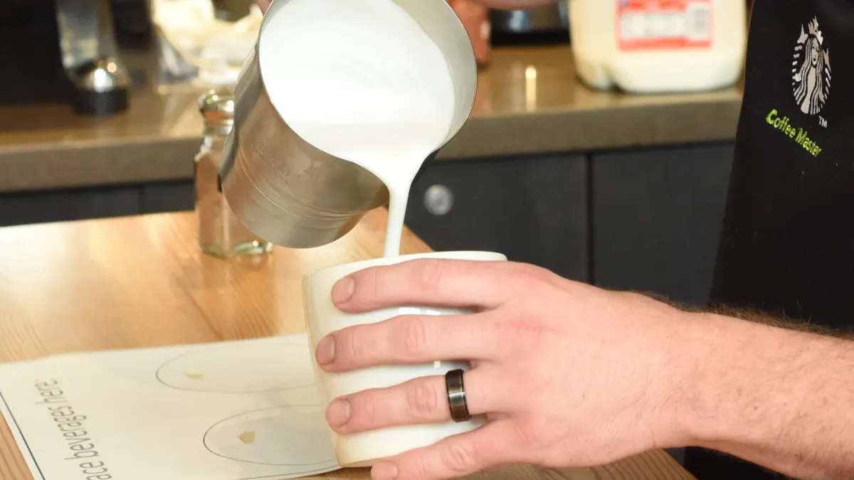 A Starbucks barista pours foamed milk into a cup.