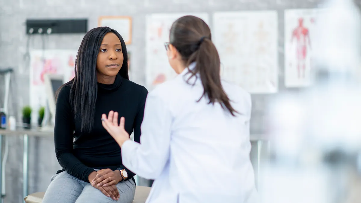 A woman of African descent and her doctor are indoors in a medical clinic.