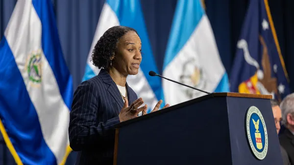 A woman in a suit stands at a podium with a Department of Labor seal on it, speaking.