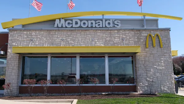 A photograh of a beige stone building with four windows out front. It has a yello face and while McDonald's logo.