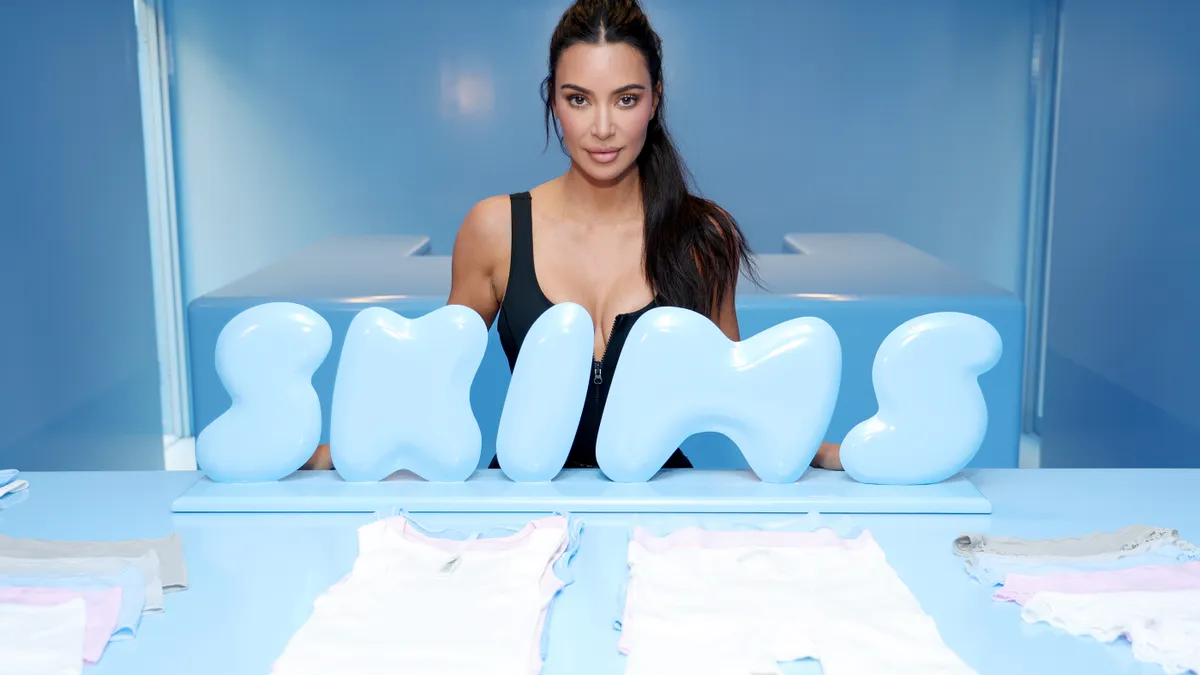 Celebrity Kim Kardashian poses behind a bright blue Skims retail product display