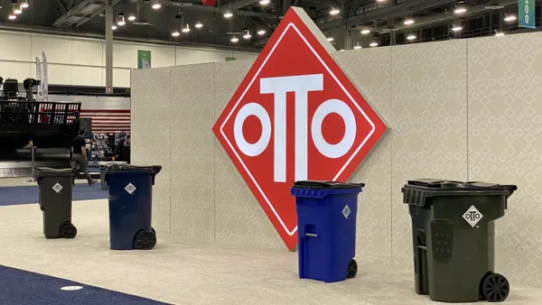 Four curbside waste and recycling bins with two wheels and a lid sit on a showroom floor in front of a large Otto sign.