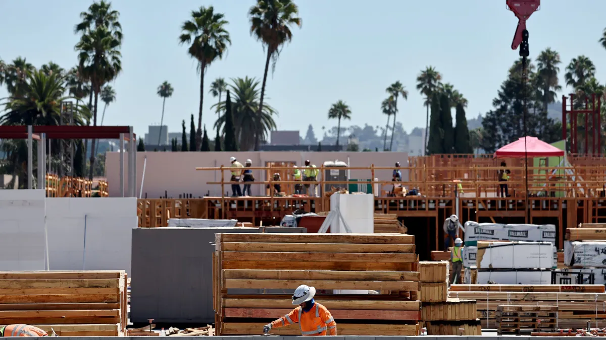 A construction worker works at a job site with palm trees in the background.