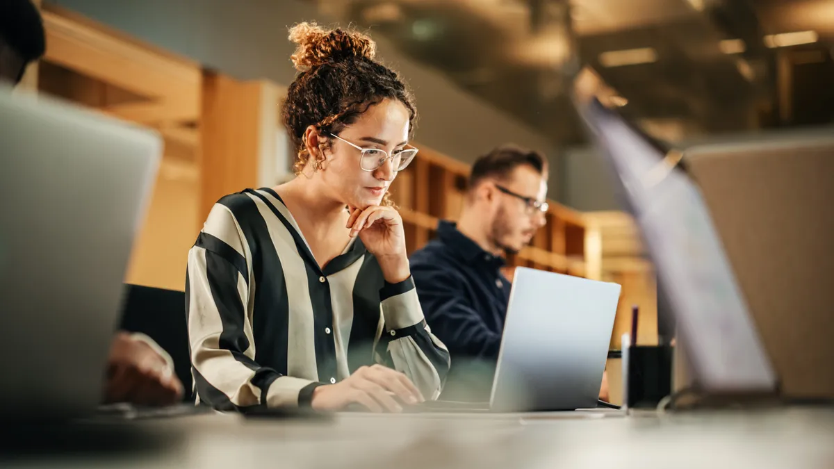 An office workers looks at a laptop screen while using a mouse