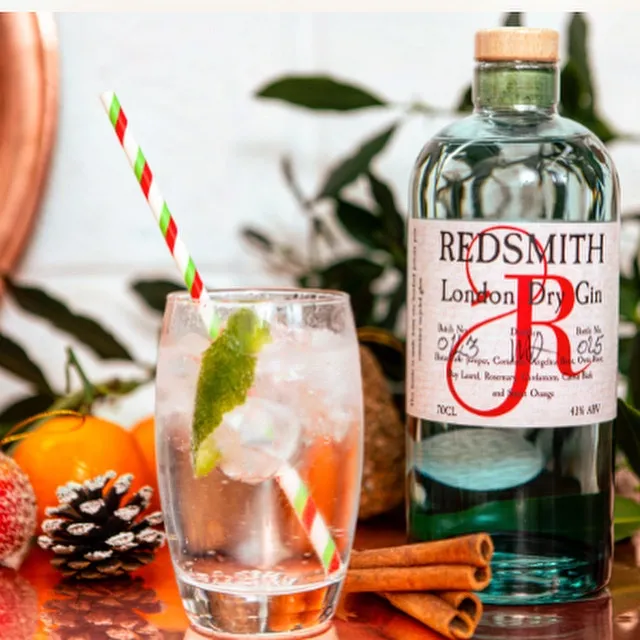 A glass containing a clear beverage and straw next to a bottle of Redsmith Distillery gin.