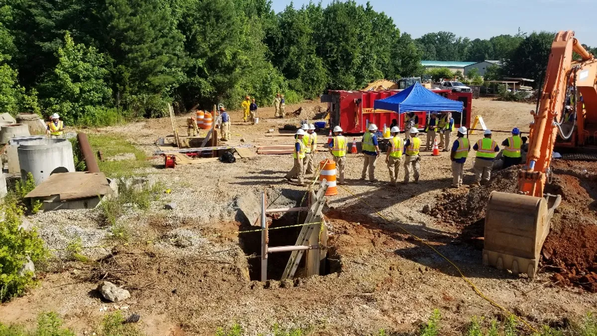 Workers in safety gear stand near tents around large holes in the ground on their jobsite.