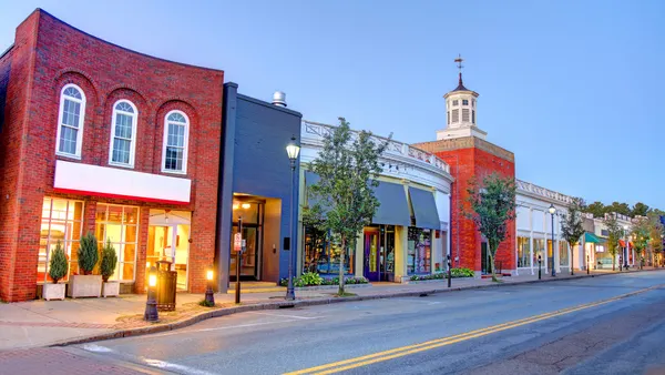 A red brick building with lights on inside sits near a quiet road on a clear day.