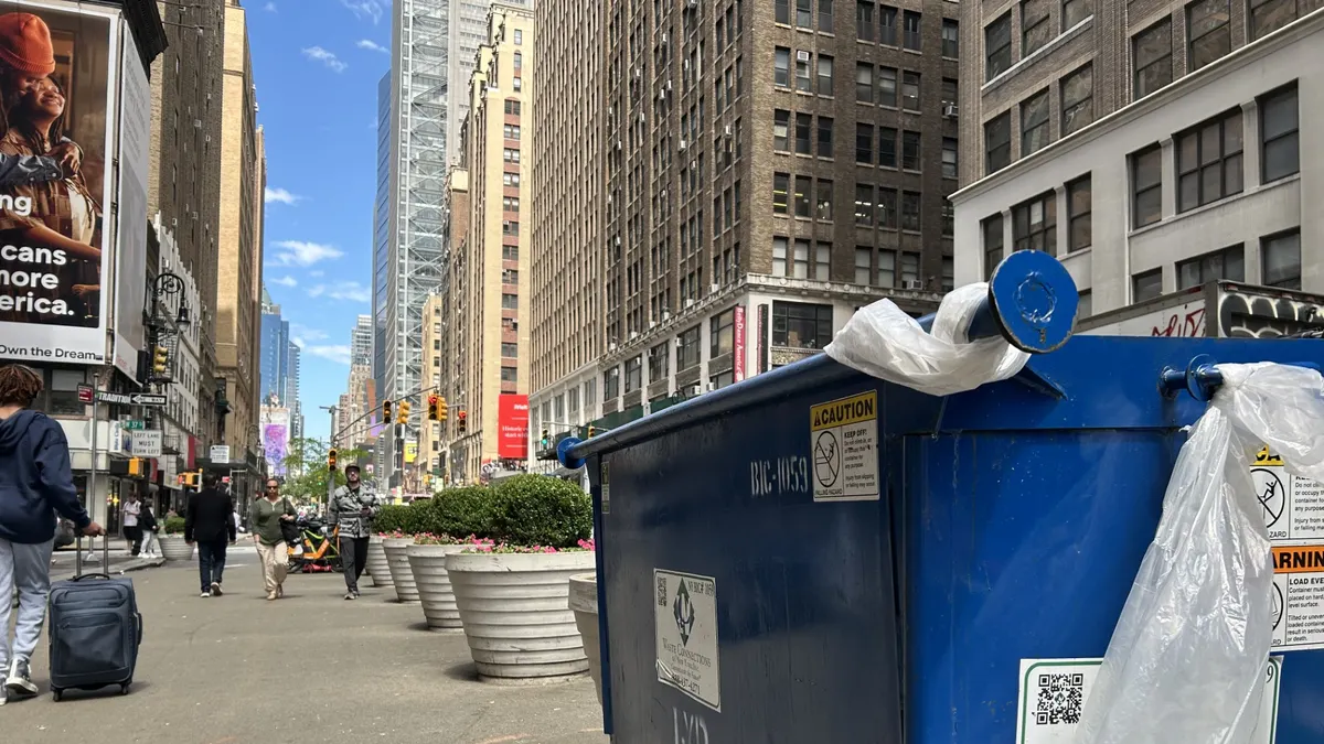 A Waste Connections dumpster on the right, New York City streetscape on the left