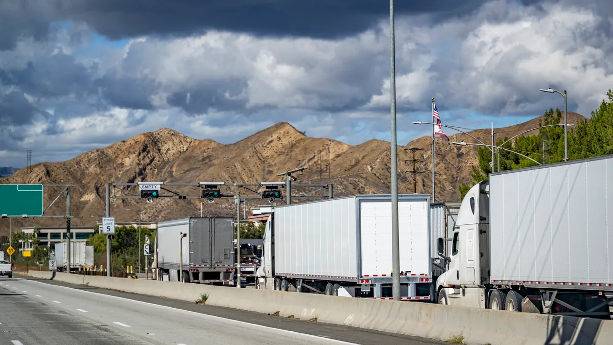 Line of big rig semi trucks with loaded semi trailers standing on the at the weighing station with scales for weighing along the axes