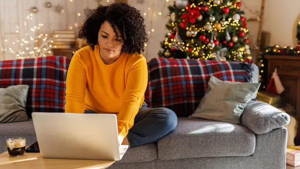 Woman sits on couch typing on laptop.