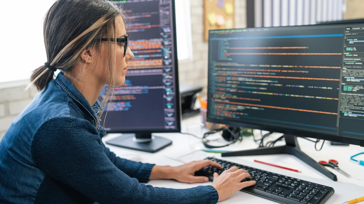 a software developer writes code while using an external monitor in an office setting