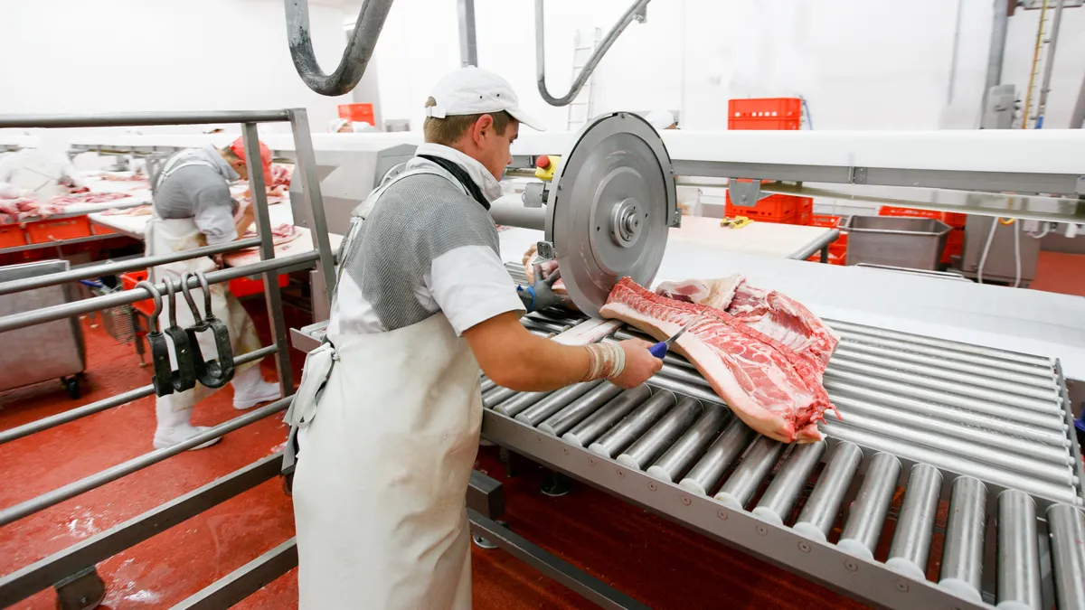 Workers chop fresh beef using industrial tools at a meat processing facility.