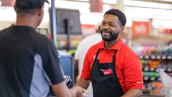 Winn-Dixie cashier wearing a red polo ringing up a customer at a grocery store checkout counter