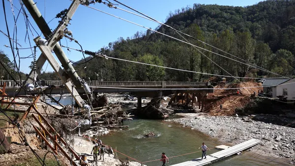 People walk across a makeshift bridge with damaged infrastructure around them.