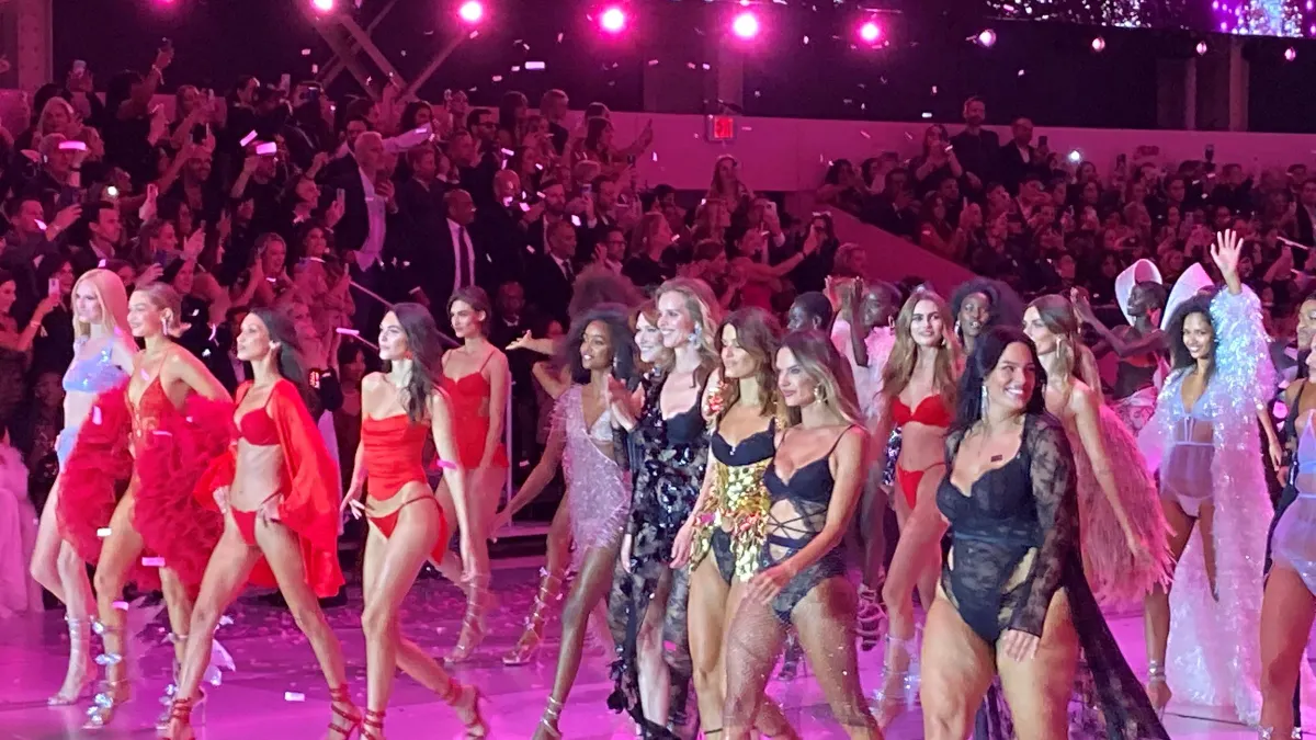 Models at the end of a runway show walk as confetti falls