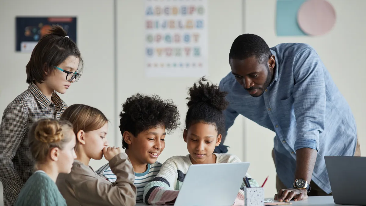 Diverse group of students working on laptop with teacher