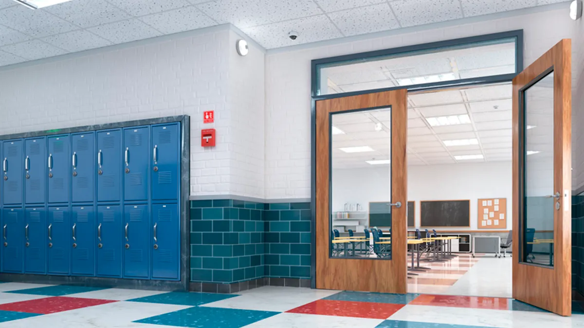 An empty hallway in a school shows lockers and a door to a classroom or cafeteria