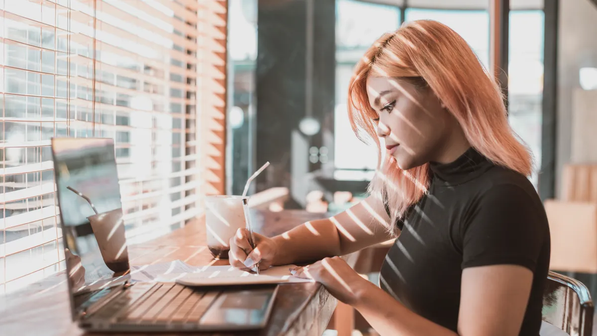 A pretty young focused professional asian woman writing down notes or making a draft. Office worker, businesswoman or freelancer at a coffee shop.