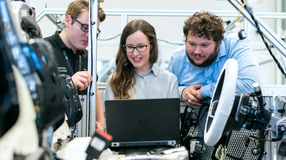 Three workers engage with a laptop in a factory, highlighting teamwork in a manufacturing environment.