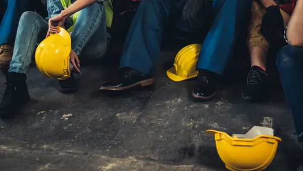 A group of people in work outfits and hard hats sit on the ground