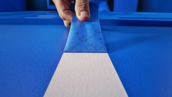 A hand pulling back blue tape to reveal a white row.