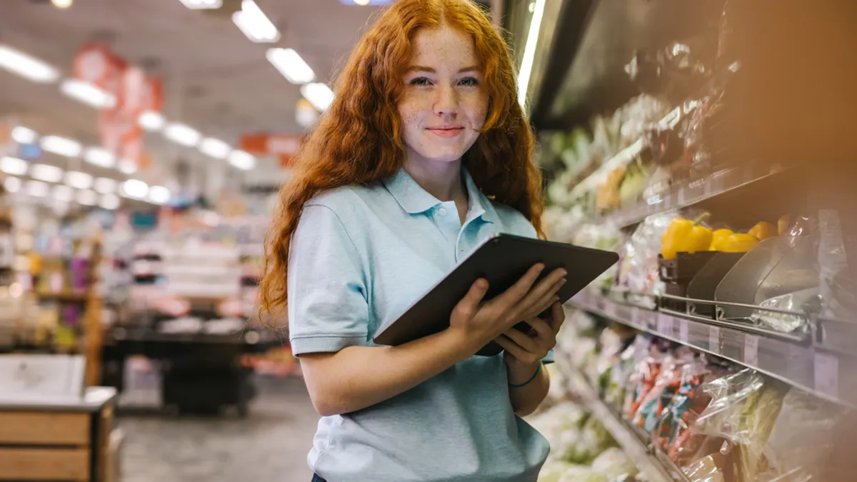 Happy woman working in a supermarket. Caucasian female grocery store employee with a digital tablet.